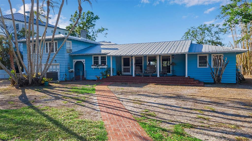 A blue, single-story house with a metal roof and a brick walkway leading to the porch — 1479 BAY POINT DRIVE, SARASOTA, FL