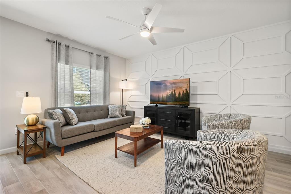 A living room features a gray sofa, patterned armchairs, a wood coffee table, and a geometric-patterned wall — 14937 HARVEST STREET, ORLANDO, FL