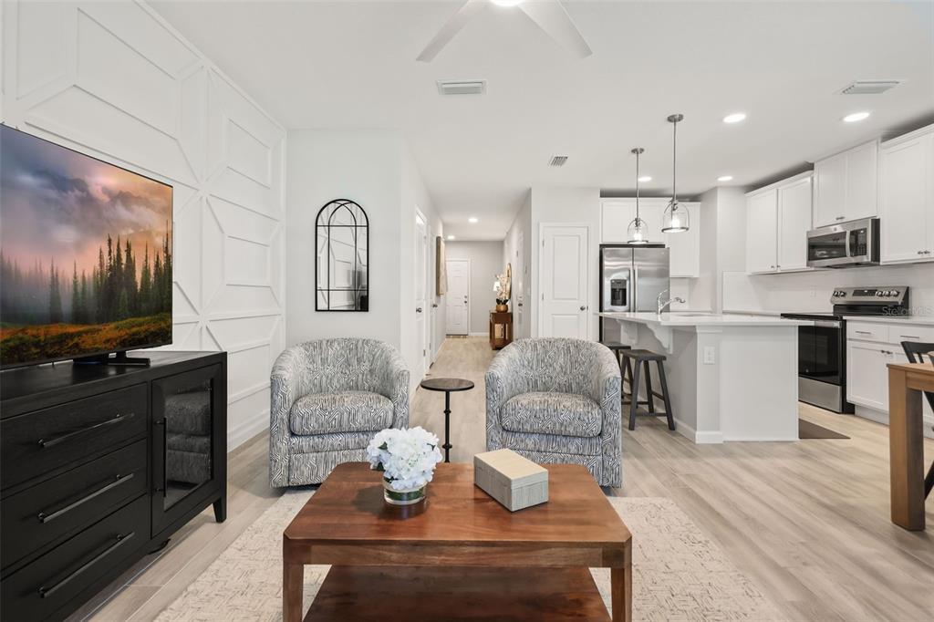 A living room with patterned armchairs and a wooden coffee table faces a modern kitchen — 14937 HARVEST STREET, ORLANDO, FL