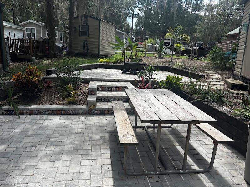 A backyard patio features paver flooring, a picnic table, tiered steps, and two storage sheds — 25244 NE 143RD  ST UNIT 180, SALT SPRINGS, FL