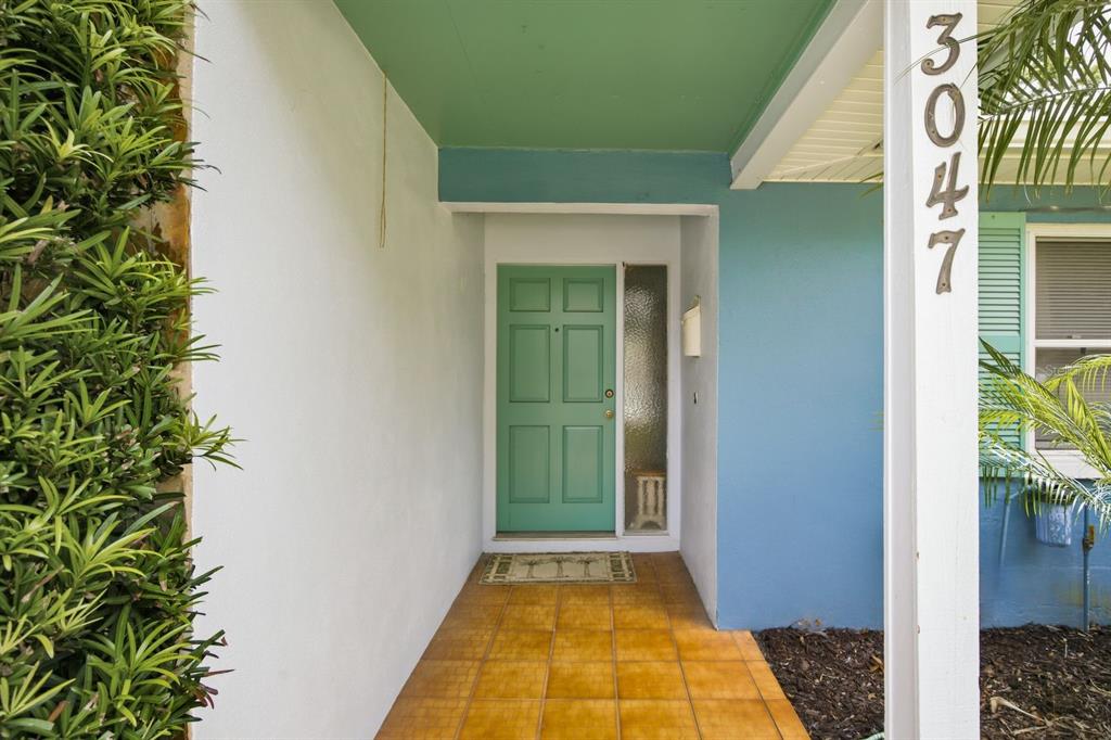 A covered entryway features a teal front door, tiled flooring, and a white house number post — 3047 CASCADE DRIVE, CLEARWATER, FL