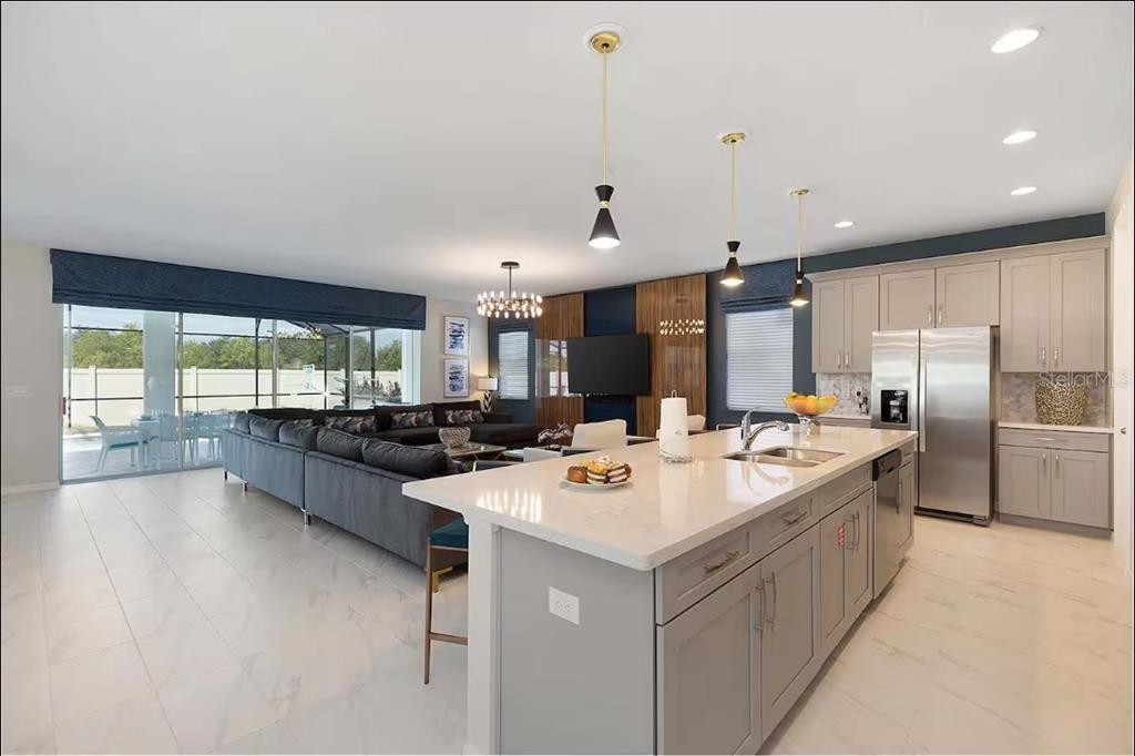 A modern open-concept kitchen and living area with gray cabinetry, a large island, and tile flooring — 1852 CARIBBEAN VIEW TERRACE, KISSIMMEE, FL