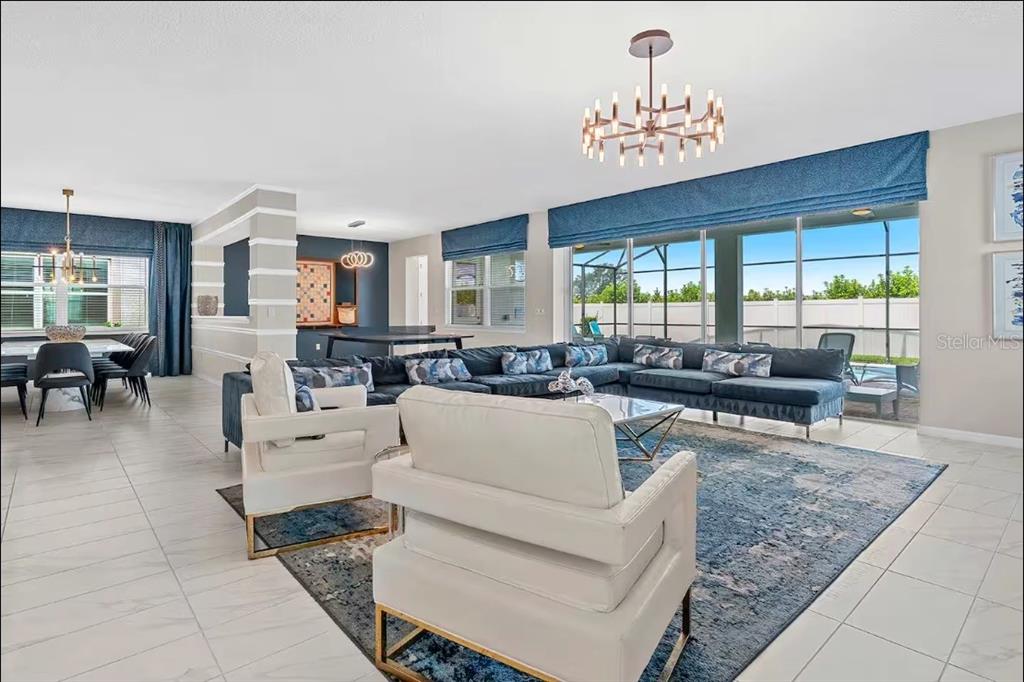 A spacious living room features a large blue sectional, white armchairs, and a modern chandelier — 1852 CARIBBEAN VIEW TERRACE, KISSIMMEE, FL