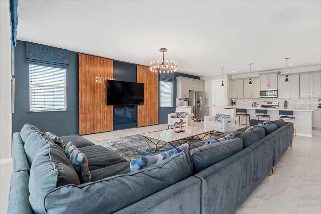 A spacious open-concept living room features a large sectional sofa, wood-paneled TV wall, and kitchen — 1852 CARIBBEAN VIEW TERRACE, KISSIMMEE, FL