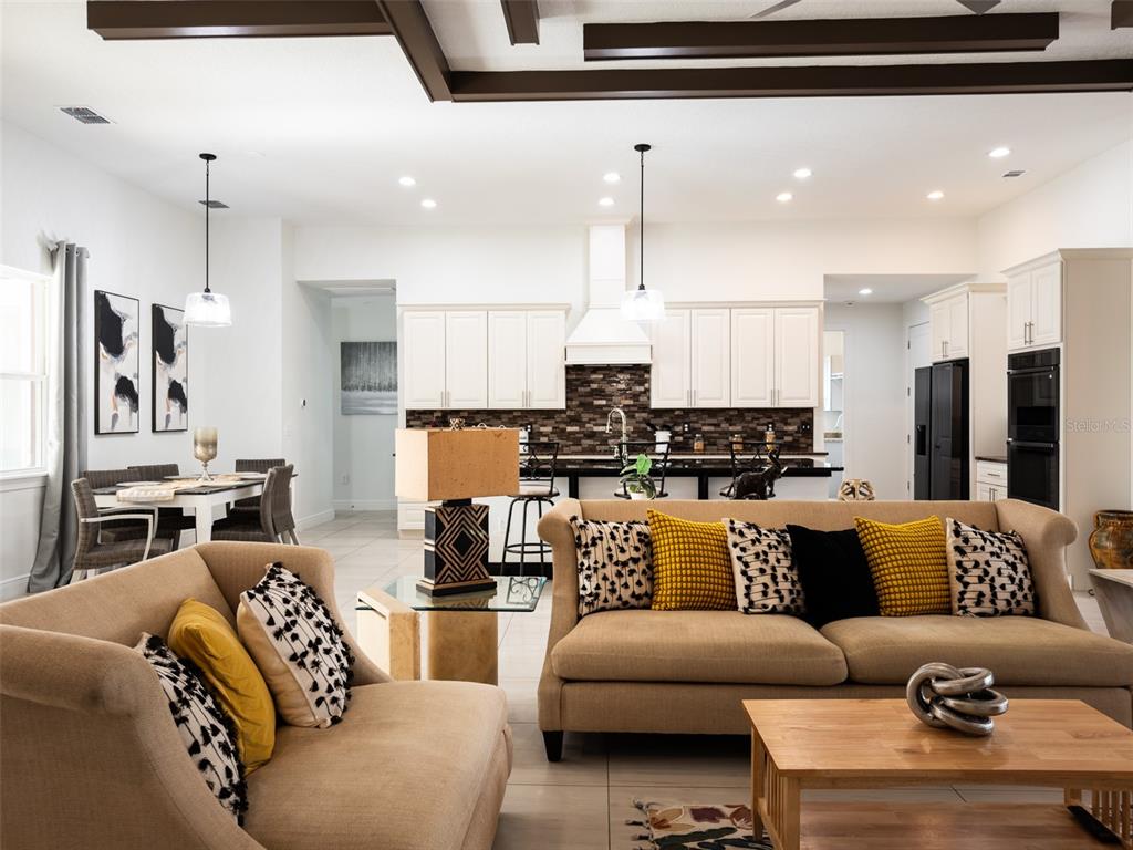 An open-concept living room and kitchen featuring neutral furniture, dark wood ceiling beams, and cabinetry — 41289 COUNTY ROAD 452, LEESBURG, FL