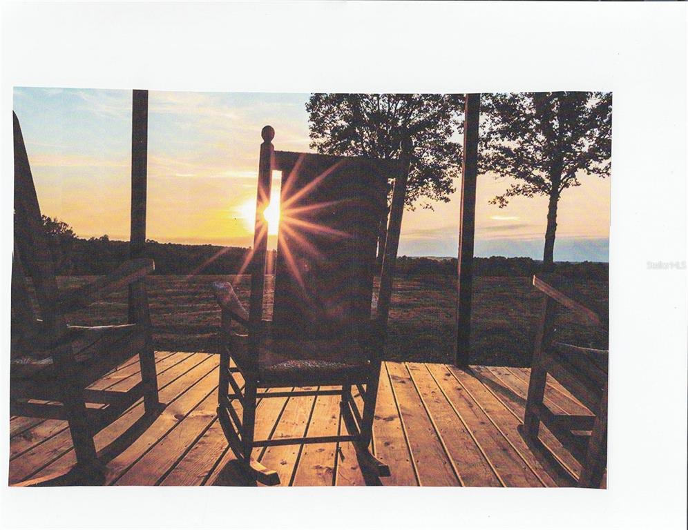 A wooden rocking chair sits on a deck overlooking a sunset over a grassy field — lot 7 SE 136TH TERRACE, DUNNELLON, FL