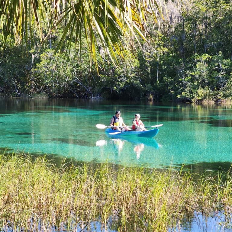 Two people paddle a blue kayak across a clear, turquoise spring surrounded by lush vegetation — lot 7 SE 136TH TERRACE, DUNNELLON, FL