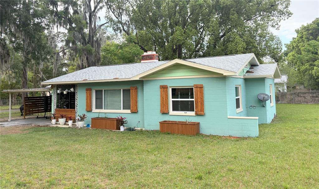 A single-story teal house with a light-colored roof, wooden shutters, and a brick chimney — 2131 NE 3RD STREET, OCALA, FL
