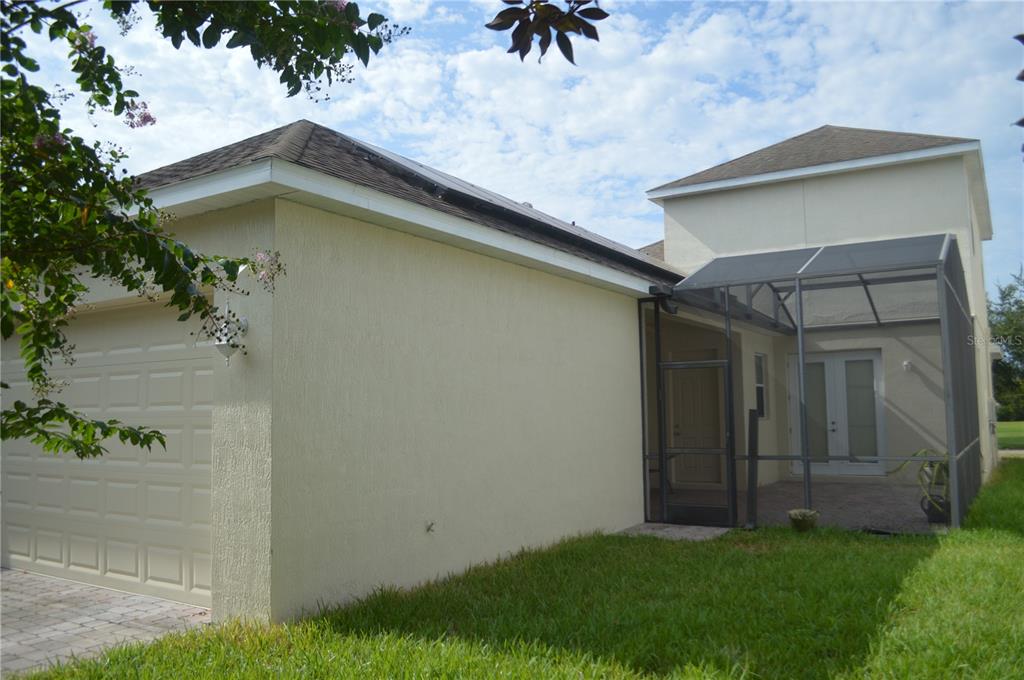 A beige house exterior featuring a garage, a screened-in patio, and a grassy lawn — 6828 HELMSLEY CIRCLE, WINDERMERE, FL