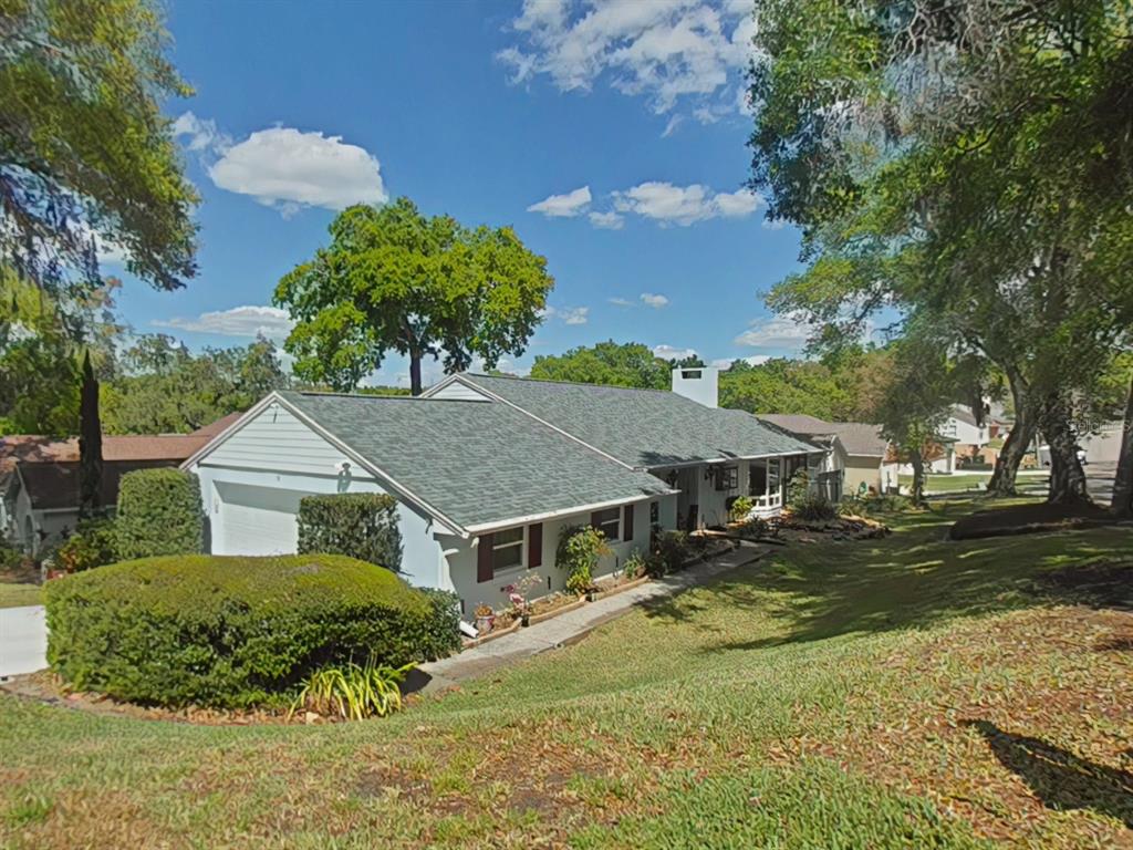 A single-story house with a gray roof and white siding sits on a grassy hill — 58 TOWNHILL DRIVE, EUSTIS, FL