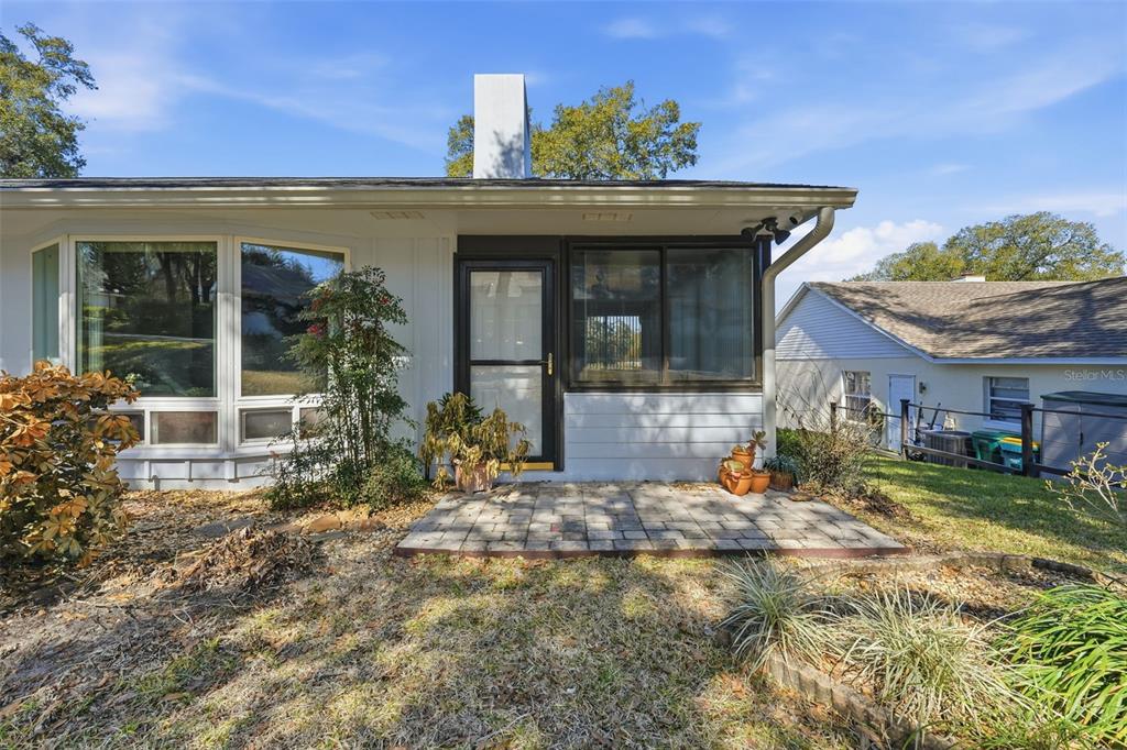 A paved patio sits in front of a house with a bay window and glass door — 58 TOWNHILL DRIVE, EUSTIS, FL