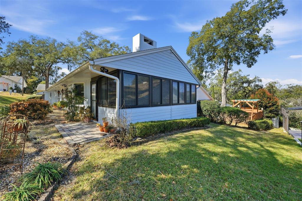 A light-colored house with a screened-in porch and a stone patio sits on a lawn — 58 TOWNHILL DRIVE, EUSTIS, FL
