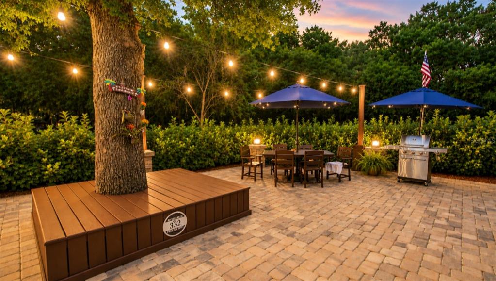A paved outdoor patio features wicker furniture, blue umbrellas, and a raised wooden platform — 332 BOBCAT LANE, LAKE WALES, FL
