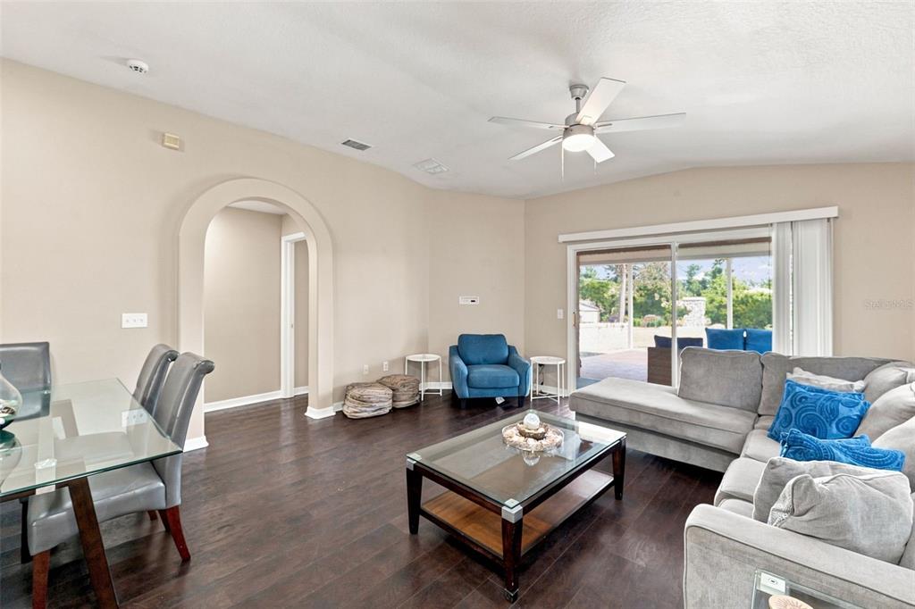 A living room and dining area with dark wood floors, a sectional sofa, and sliding doors — 6817 ARAMON COURT, WESLEY CHAPEL, FL