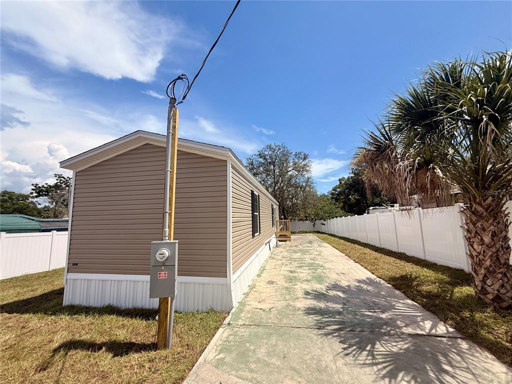 A tan mobile home exterior features a wooden staircase leading to a white entry door — 9024 KOSIMO STREET, NEW PORT RICHEY, FL