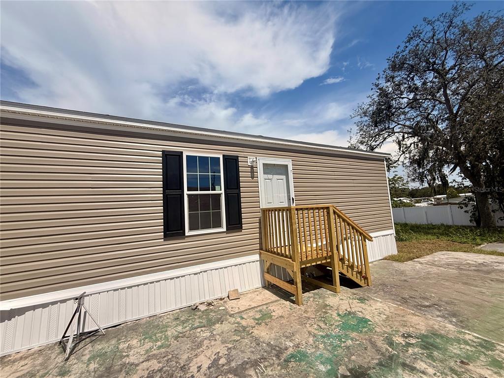A tan mobile home with a wooden staircase sits beside a driveway and white fence — 9024 KOSIMO STREET, NEW PORT RICHEY, FL