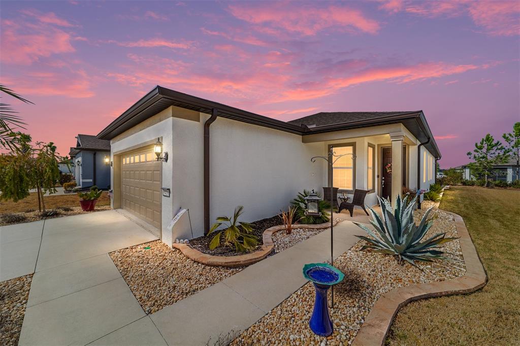 A single-story house with a tan garage, concrete walkway, and desert landscaping at sunset — 9419 SW 53RD PLACE, OCALA, FL