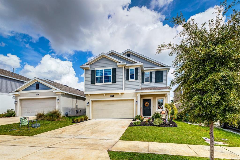 A two-story suburban house with light blue siding, a two-car garage, and a front lawn — 5571 BRAKEN FERN WAY, LEESBURG, FL