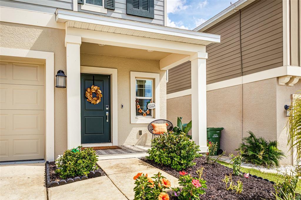 The exterior of a house features a covered front porch, a dark door, and landscaping — 5571 BRAKEN FERN WAY, LEESBURG, FL