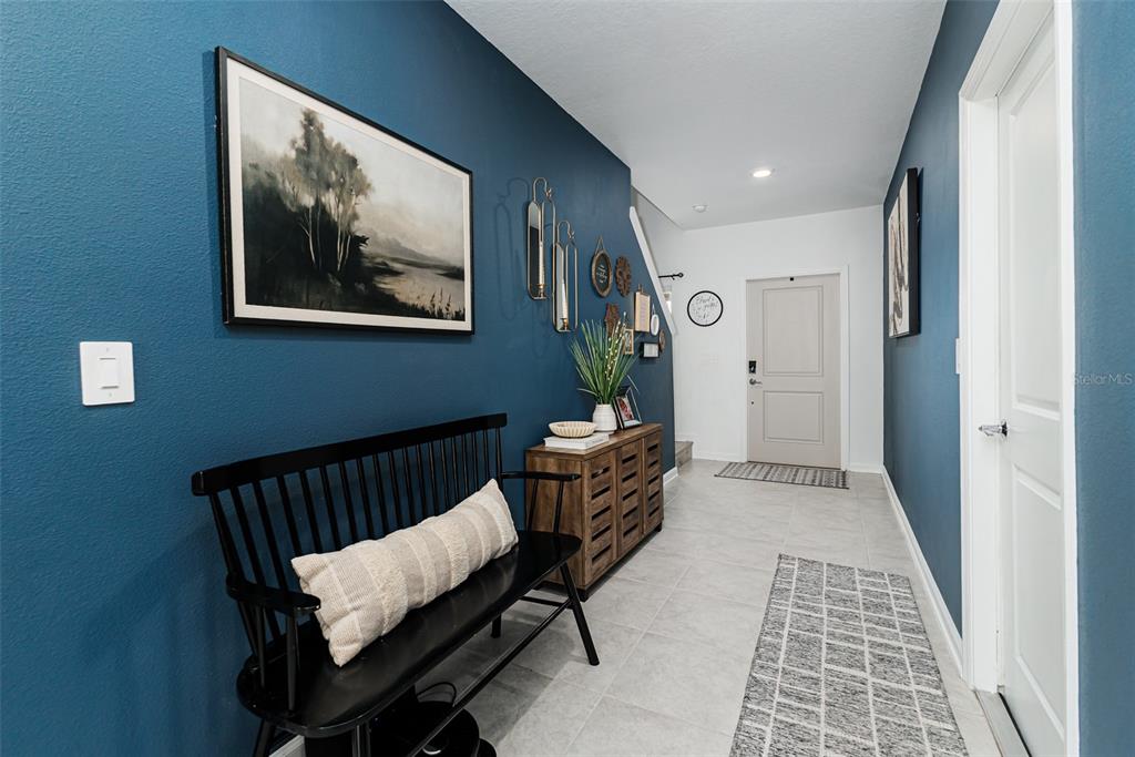 A hallway features blue walls, a black bench, a wooden console table, and tile flooring — 5571 BRAKEN FERN WAY, LEESBURG, FL