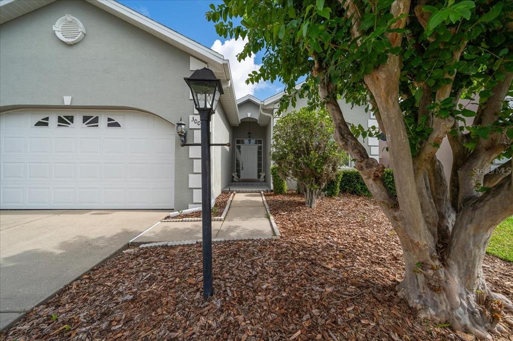A view of a house exterior featuring a garage, a walkway, and a large tree — 3003 SW 41ST PLACE, OCALA, FL