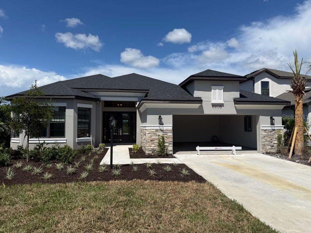 A single-story house exterior features a gray stucco facade, stone accents, and a dark roof — 8208 SUMMER NIGHT ROAD, SARASOTA, FL