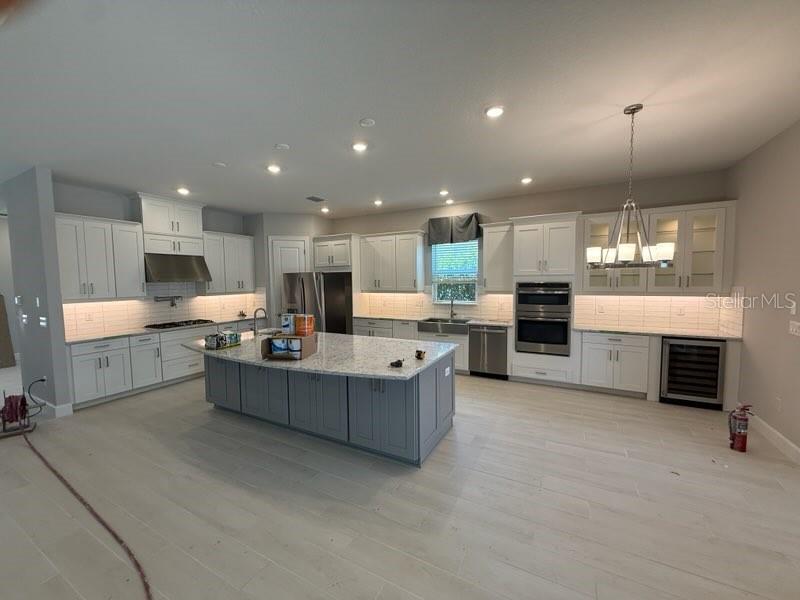 A kitchen with white cabinets, a gray island, stainless steel appliances, and light wood flooring — 8208 SUMMER NIGHT ROAD, SARASOTA, FL