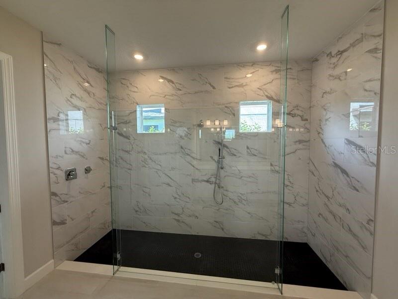 A walk-in shower features white marble-look wall tiles, a black tiled floor, and glass panels — 8208 SUMMER NIGHT ROAD, SARASOTA, FL