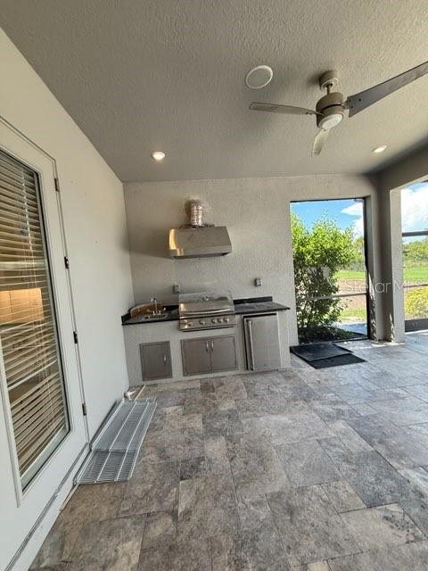 An outdoor kitchen features a stainless steel grill, range hood, and tile flooring — 8208 SUMMER NIGHT ROAD, SARASOTA, FL
