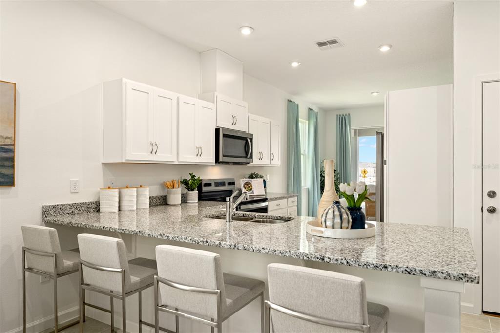 A kitchen features white cabinets, granite countertops, a breakfast bar with stools, and stainless appliances — 172 RAINWOOD STREET, GROVELAND, FL