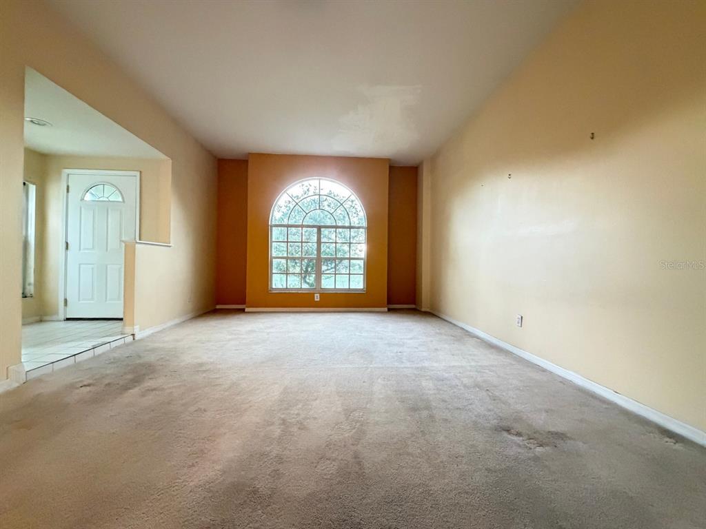 An empty living room features beige carpeting, tan walls, and a large arched window — 24449 PAINTER DRIVE, LAND O LAKES, FL
