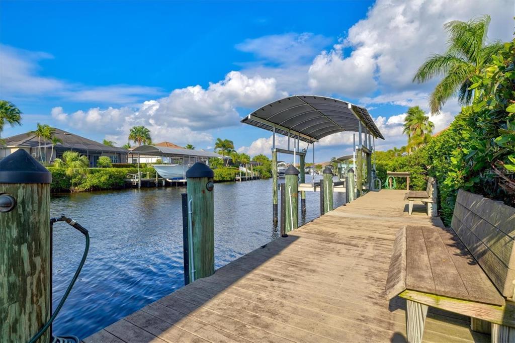 A wooden dock extends over a canal toward a covered boat lift and residential homes — 540 FORE DRIVE, BRADENTON, FL