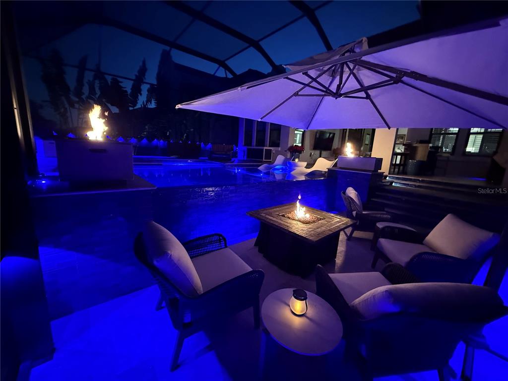 A patio at night features a fire pit, lounge chairs, a pool, and an umbrella — 1075 SEAGRAPE DRIVE, RUSKIN, FL