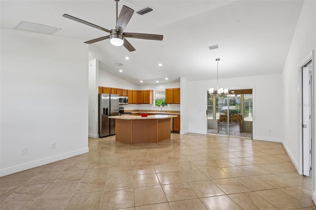 An open-concept kitchen with wood cabinets and a central island overlooks a tiled living area — 1000 KENOVA AVENUE, THE VILLAGES, FL