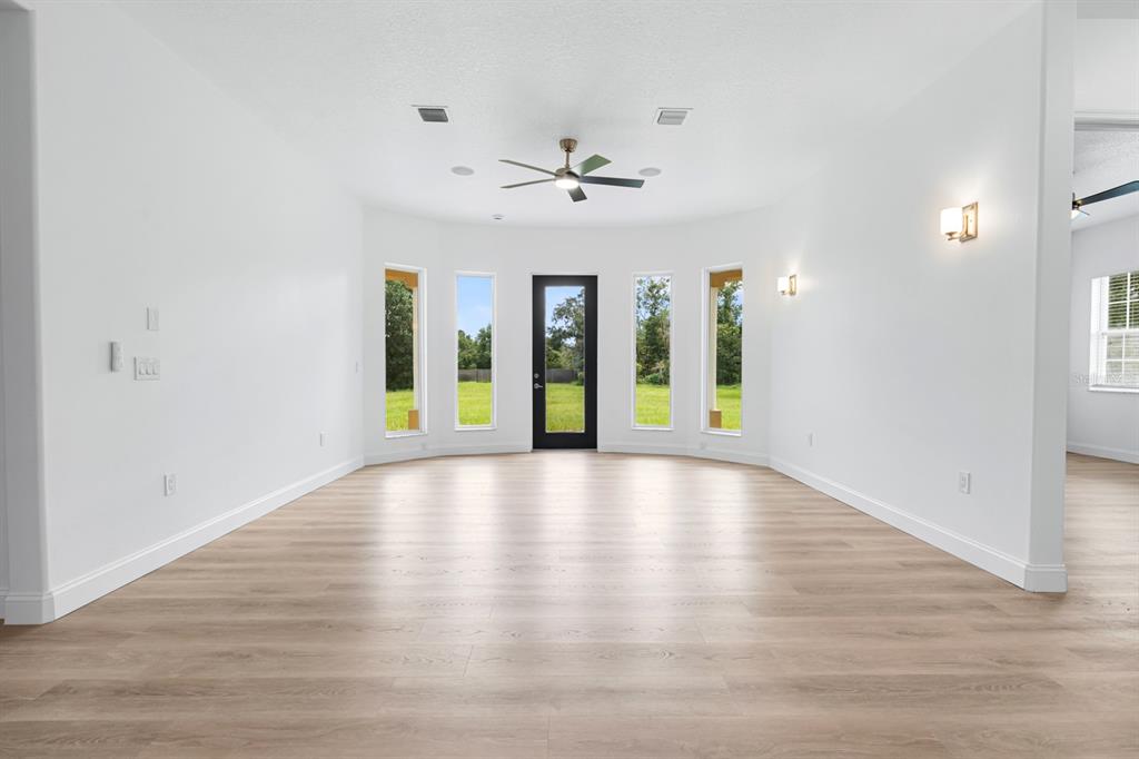 A bright, empty living room with light wood-look flooring, white walls, and a glass door — 11250 MCMULLEN ROAD, RIVERVIEW, FL
