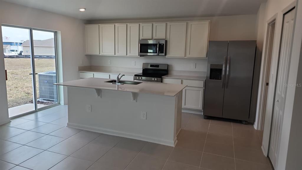 A kitchen features white cabinets, stainless steel appliances, a center island, and tile flooring — 2189 LASSO LOOP, EAGLE LAKE, FL