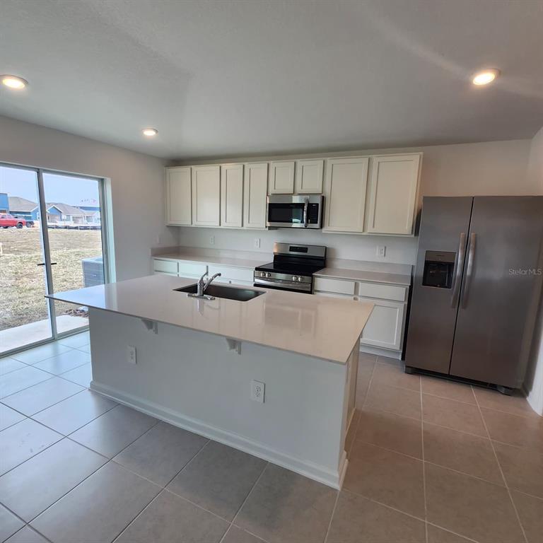 A kitchen features white cabinets, stainless steel appliances, a center island, and tile flooring — 2189 LASSO LOOP, EAGLE LAKE, FL