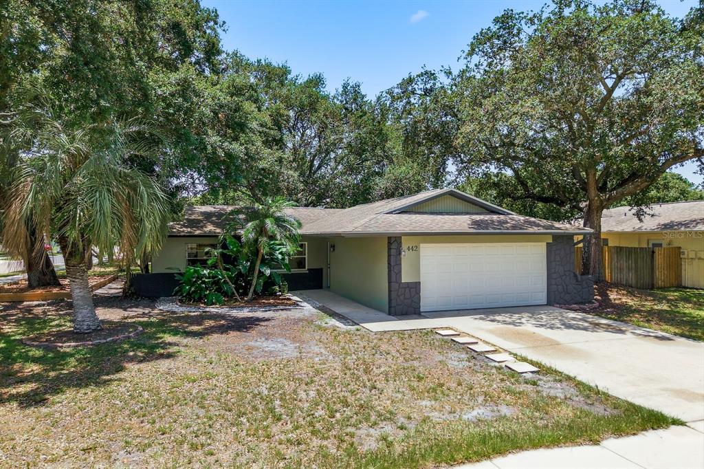 A detached garage with a white door and gray stone accents sits under large trees — 442 EVERGREEN DRIVE, OLDSMAR, FL
