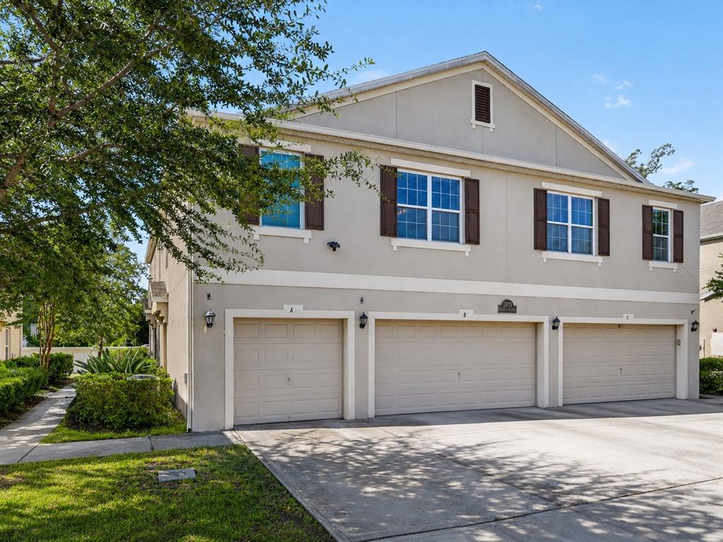 A three-unit townhouse building with beige stucco siding, brown shutters, and three garage doors — 3771 SENECA CLUB LOOP UNIT 59-101 A, ORLANDO, FL