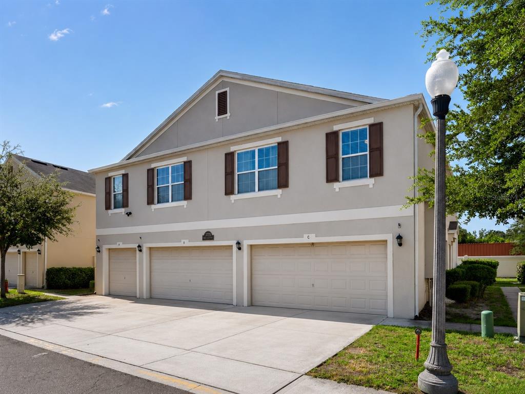 A three-car garage building with beige stucco siding and brown shutters under a clear sky — 3771 SENECA CLUB LOOP UNIT 59-101 A, ORLANDO, FL