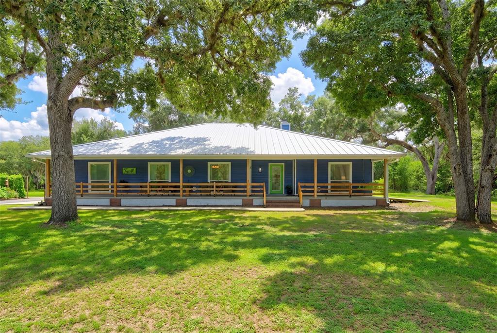 A blue-sided porch features wicker chairs, a green "Faith" sign, and a wooden railing — 9990 SW COUNTY ROAD 769, ARCADIA, FL