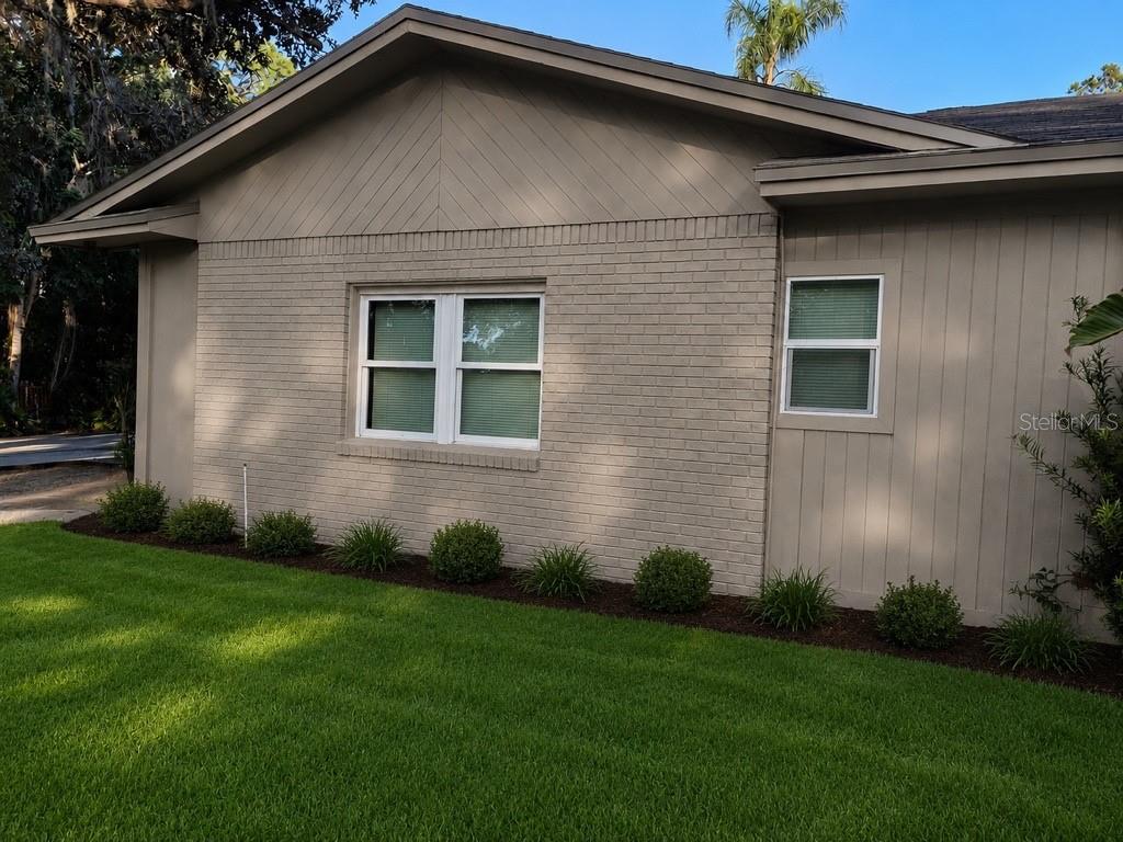 A tan brick and vertical siding house exterior features a large window and manicured landscaping — 4327 PLYMOUTH SORRENTO ROAD, APOPKA, FL