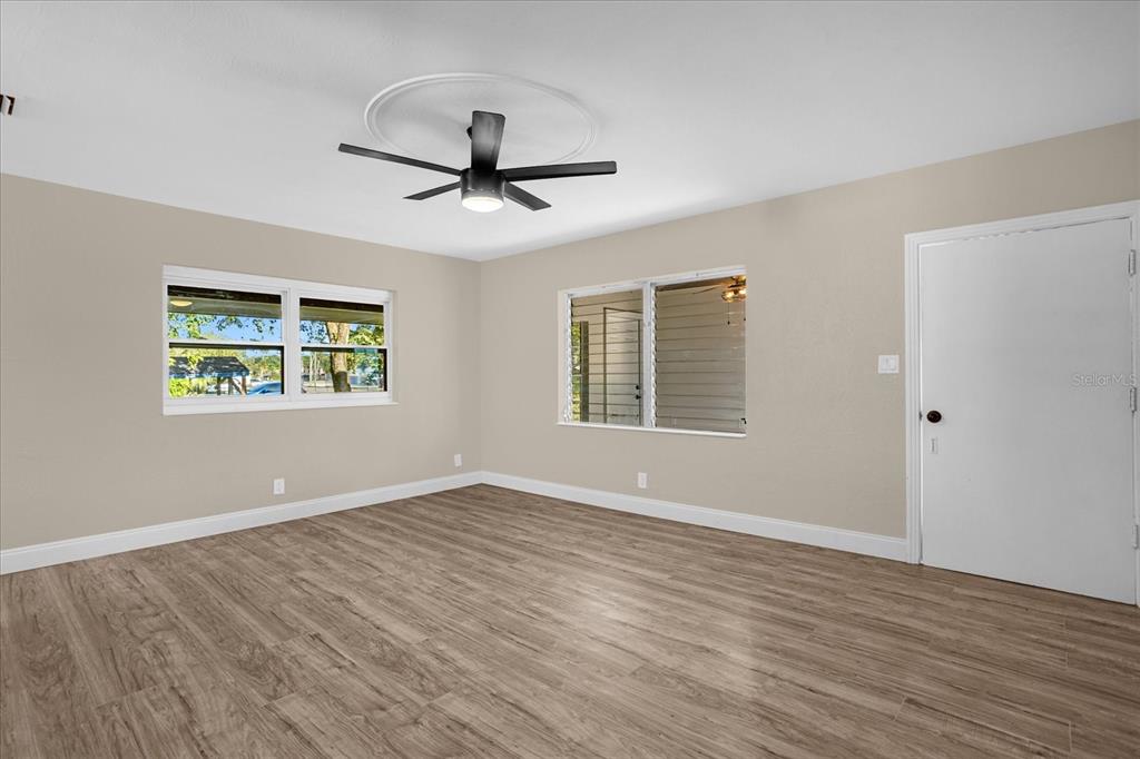 An empty room features light wood-look flooring, beige walls, two windows, and a ceiling fan — 1008 10TH STREET, DAYTONA BEACH, FL