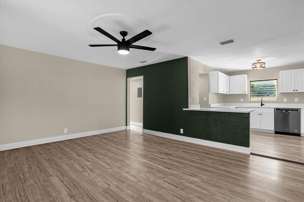 A living room with wood-look flooring and a ceiling fan opens to a white kitchen — 1008 10TH STREET, DAYTONA BEACH, FL