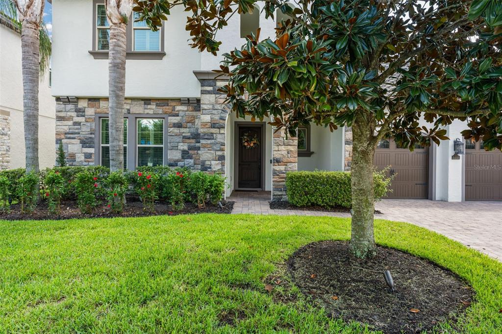 A two-story house exterior features a stone facade, a front door, and a landscaped yard — 8498 MOREHOUSE DRIVE, ORLANDO, FL