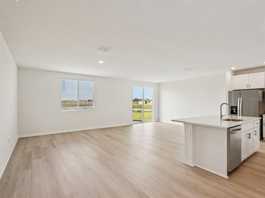 A bright, open-concept living area features light wood-look flooring, a kitchen island, and sliding doors — 10417 ABUNDANCE GROVE WAY, PARRISH, FL