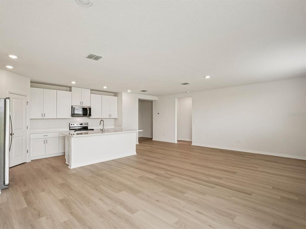A bright kitchen with white cabinets and an island opens into a spacious living area — 10417 ABUNDANCE GROVE WAY, PARRISH, FL