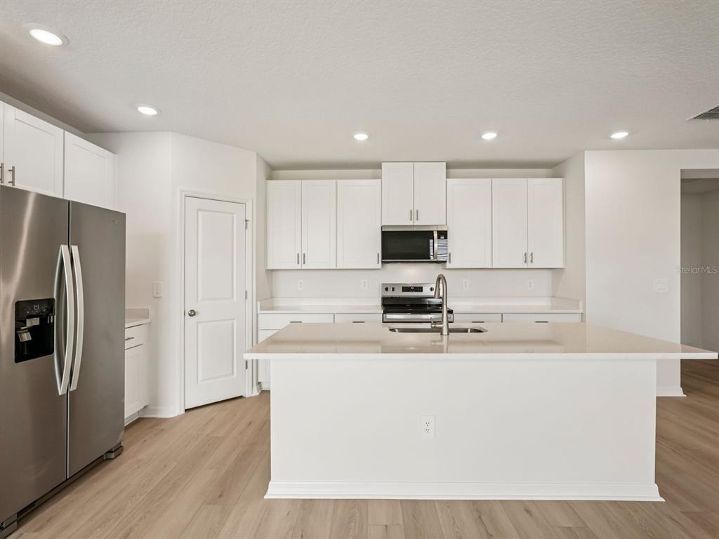 A modern kitchen features white cabinets, stainless steel appliances, and a large central island — 10417 ABUNDANCE GROVE WAY, PARRISH, FL