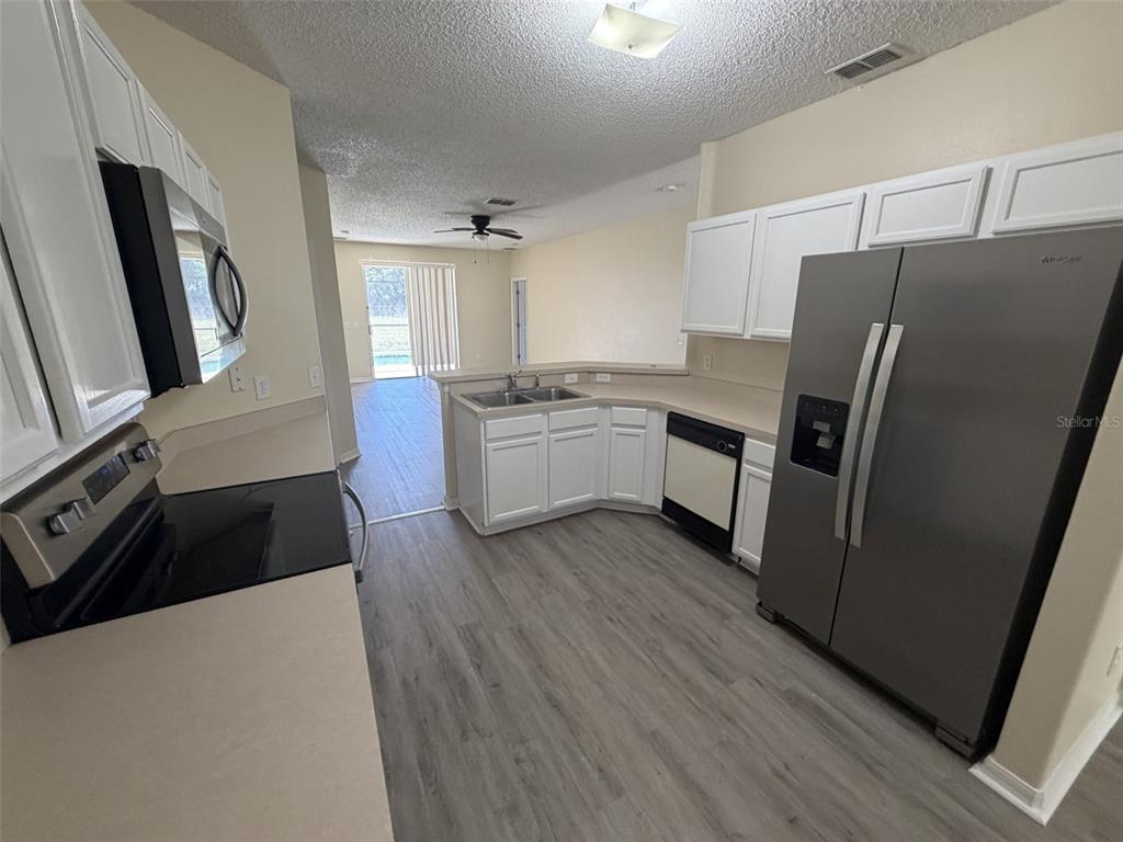 A kitchen with white cabinets, stainless steel appliances, and wood-look flooring opens to a living area — 311 SUNSET VIEW DRIVE, DAVENPORT, FL