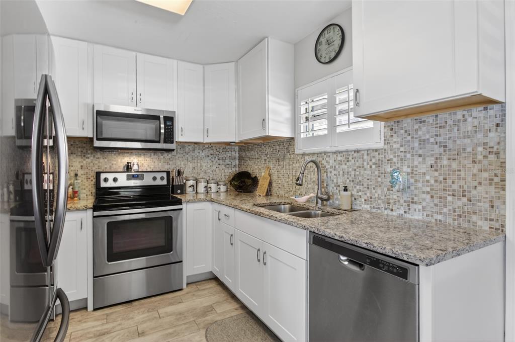 A kitchen features white cabinets, granite countertops, stainless steel appliances, and a mosaic tile backsplash — 105 CENTRAL AVENUE, CRESCENT CITY, FL